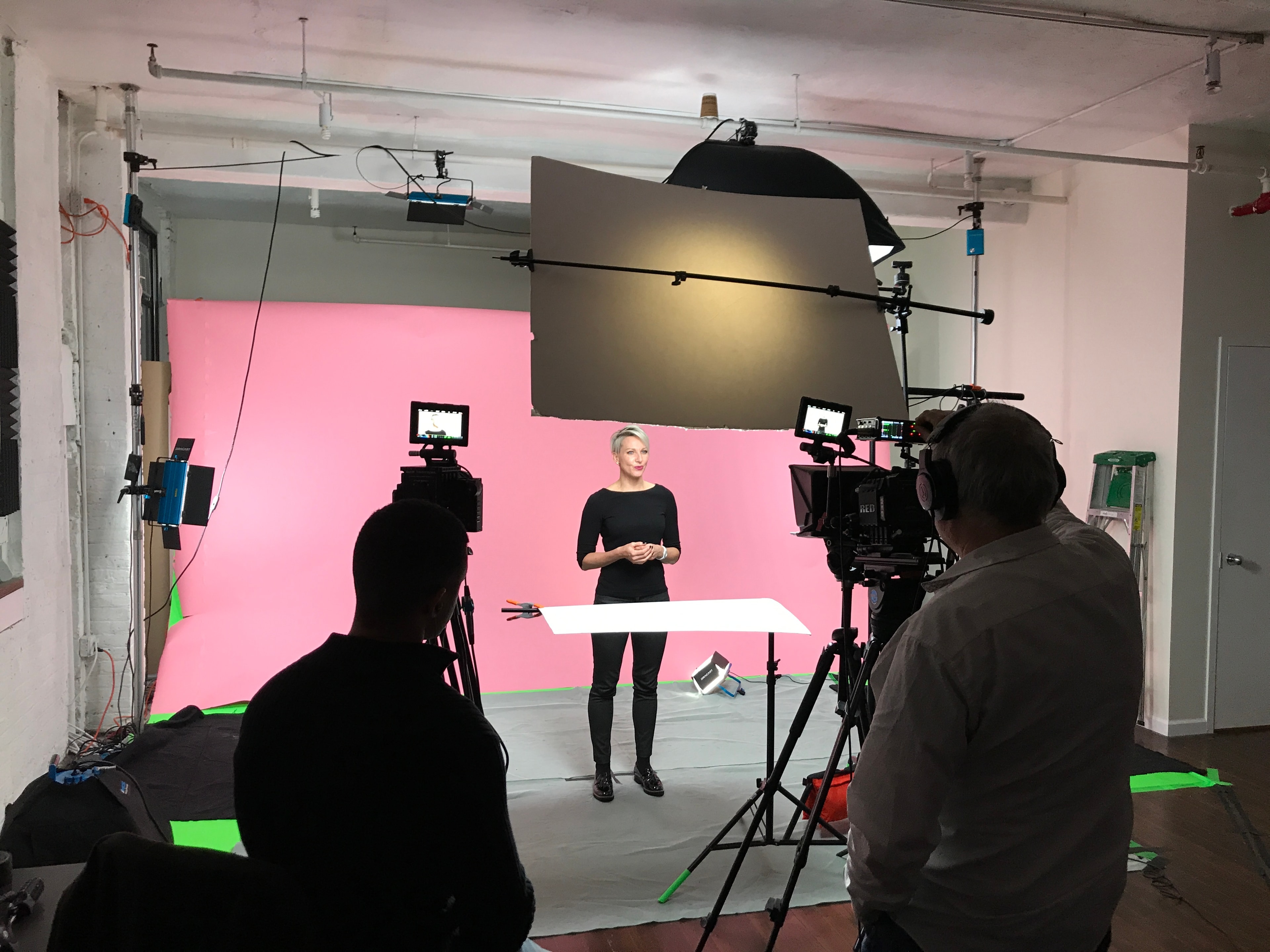 Behind-the-scenes studio production with a presenter on a pink set